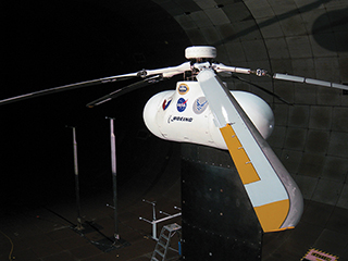 Side-view of a test helicopter in a wind tunnel with a focus on one of the blades. Side-view of a test helicopter in a wind tunnel with a focus on one of the blades.