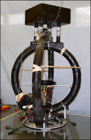 A photo of an electromagnetic device. It looks like a spokeless unicycle with another ring crossecting it and wires connected to it. A photo of an electromagnetic device. It looks like a spokeless unicycle with another ring crossecting it and wires connected to it.
