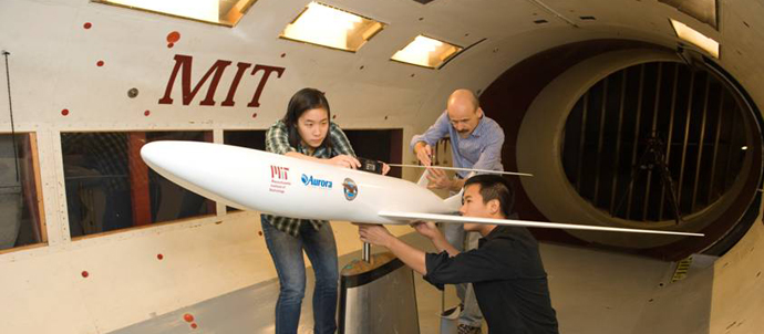 A woman and two men examine and take measurements of a model jet inside a wind tunnel. A woman and two men examine and take measurements of a model jet inside a wind tunnel.