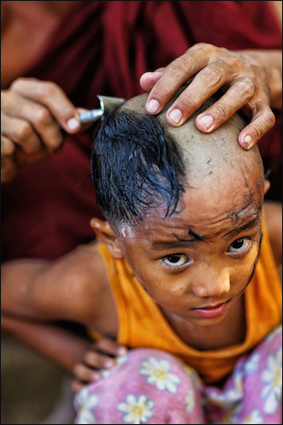 A photograph of a young Burmese boy who is in the middle of having his head shaved by an older monk. A photograph of a young Burmese boy who is in the middle of having his head shaved by an older monk.