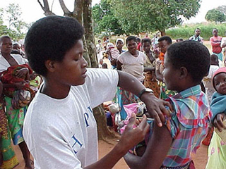 A woman receiving a vaccination at a street clinic as others watch. A woman receiving a vaccination at a street clinic as others watch.