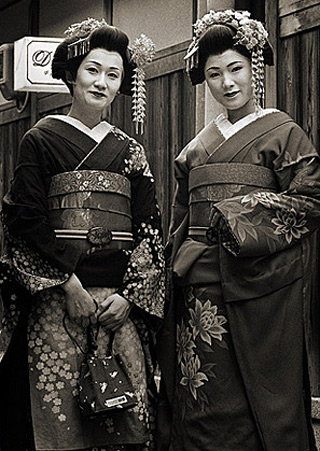A black and white photograph of two women dressed as geishas. A black and white photograph of two women dressed as geishas.