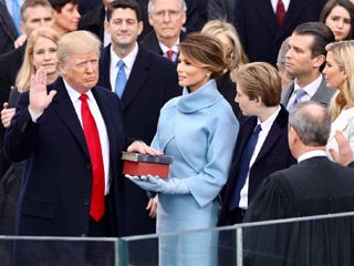 With his right hand raised in the air, an old, reddish-grey haired man rests his left hand on a Bible held by an elegantly-dressed young woman. With his right hand raised in the air, an old, reddish-grey haired man rests his left hand on a Bible held by an elegantly-dressed young woman.