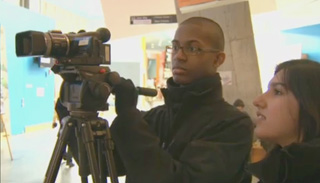 Two students working with a tripod-mounted video camera. Two students working with a tripod-mounted video camera.