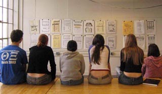 Six students sit on the edge of a table reviewing each others work. Six students sit on the edge of a table reviewing each others work.