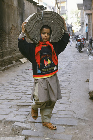 A young boy in India walks while carrying a tied up bundle of punched-data cards on his head. A young boy in India walks while carrying a tied up bundle of punched-data cards on his head.