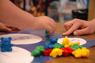 A child sorts colorful toy bears as a teacher looks on. A child sorts colorful toy bears as a teacher looks on.