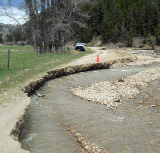 Photo of a gravel road washed away by curving creekbed. Photo of a gravel road washed away by curving creekbed.