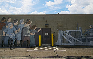 A photo of a mural depicting a group of people standing in front of a bulldozer. The bulldozer reads "Federal Inner Belt I-95". A photo of a mural depicting a group of people standing in front of a bulldozer. The bulldozer reads "Federal Inner Belt I-95".