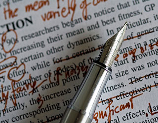 A silver fountain pen rests on top of a paper marked with edits in red ink. A silver fountain pen rests on top of a paper marked with edits in red ink.