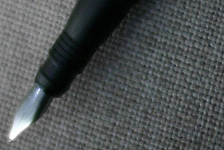 Photograph of a fountain pen in front of a grey fabric background. Photograph of a fountain pen in front of a grey fabric background.