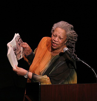 Toni Morrison holds up a book while she speaks at a lectern. Toni Morrison holds up a book while she speaks at a lectern.