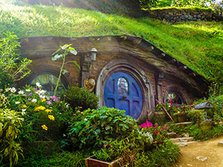 A photograph of a tiny house tucked into the side of a grassy hill surrounded by flowers. A photograph of a tiny house tucked into the side of a grassy hill surrounded by flowers.