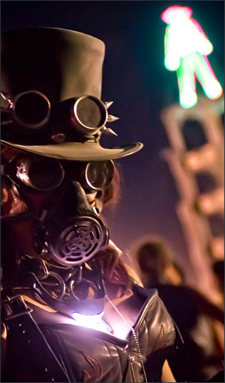 Woman in a top hat, spiked goggles, gas mask, glowing necklace, chain, and leather top, in front of a bright humanoid shape that stands atop a tall tower. Woman in a top hat, spiked goggles, gas mask, glowing necklace, chain, and leather top, in front of a bright humanoid shape that stands atop a tall tower.