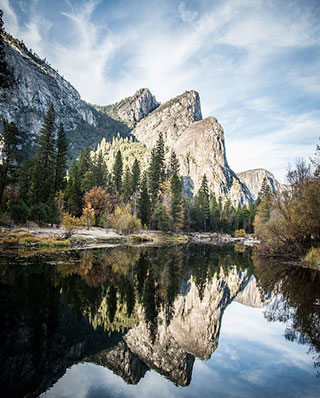 A photograph of a rock formation known as "Three Brothers" at Yosemite National Park. The rock formation is surrounded by trees and reflected in a body of water in the foreground. A photograph of a rock formation known as "Three Brothers" at Yosemite National Park. The rock formation is surrounded by trees and reflected in a body of water in the foreground.