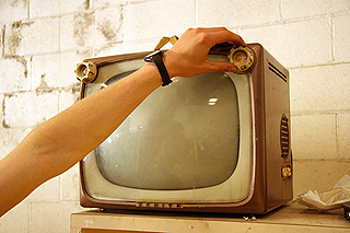 A hand turns on a small vintage television set. A hand turns on a small vintage television set.