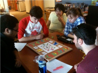 Five students sit around a table, playing a board game. Five students sit around a table, playing a board game.
