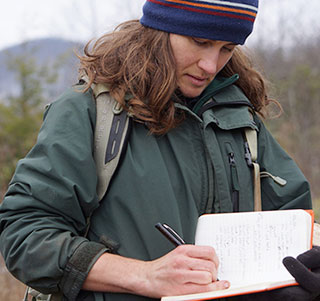 A woman takes notes while standing in a field. A woman takes notes while standing in a field.