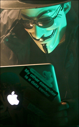 Disguised by the mask of Guy Fawkes, the Anonymous Hacker peers at his laptop screen through black glasses. Disguised by the mask of Guy Fawkes, the Anonymous Hacker peers at his laptop screen through black glasses.
