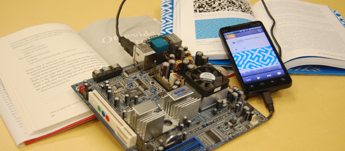 A smart phone connected to a circuit board lay on top of two open books. A smart phone connected to a circuit board lay on top of two open books.