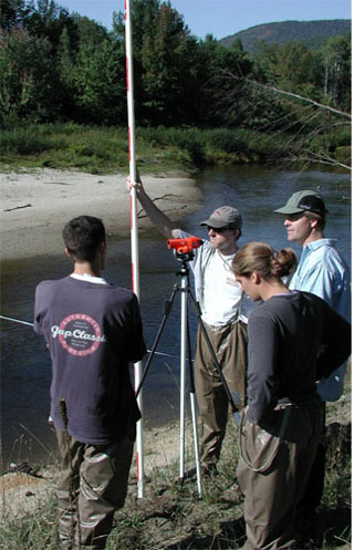 Four people with survey equipment near a river. Four people with survey equipment near a river.