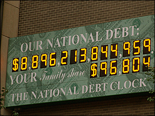 A photograph of a billboard sized electronic clock on a brick wall that displays the national debt of the United States. A photograph of a billboard sized electronic clock on a brick wall that displays the national debt of the United States.