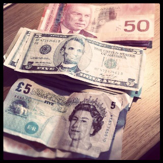 A photograph of stacks of Canadian fifty dollar, American five dollar, and British five pound notes lined up on a table. A photograph of stacks of Canadian fifty dollar, American five dollar, and British five pound notes lined up on a table.
