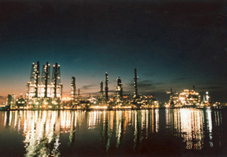 Photo of a refinery lit at night, reflected in water. Photo of a refinery lit at night, reflected in water.