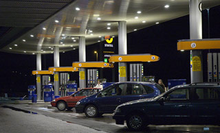 At night, cars fill up at a multi-lane gas station. At night, cars fill up at a multi-lane gas station.