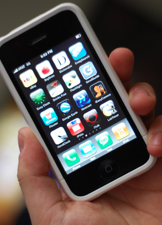 Photograph of a hand holding an Apple iPhone displaying a screen of icons for various apps. Photograph of a hand holding an Apple iPhone displaying a screen of icons for various apps.