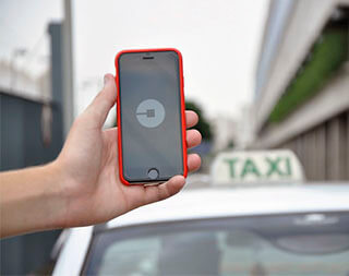Someone holds a smartphone with an Uber app open on it. A taxi is seen in the background. Someone holds a smartphone with an Uber app open on it. A taxi is seen in the background.