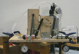 A hand-powered vacuum pump features a wooden flywheel that connects to two commercial vacuum pump units, mounted on a wooden frame. A hand-powered vacuum pump features a wooden flywheel that connects to two commercial vacuum pump units, mounted on a wooden frame.