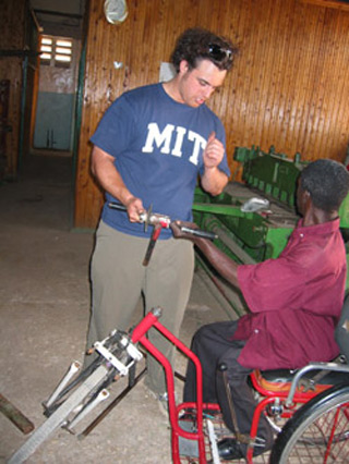 Man sitting in a three-wheeled chair, holding the hand crank component. Man sitting in a three-wheeled chair, holding the hand crank component.