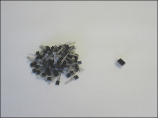 Photograph of a pile of 100 tiny discrete transistors next to an equally tiny 100 integrated transistors which are a single piece. Photograph of a pile of 100 tiny discrete transistors next to an equally tiny 100 integrated transistors which are a single piece.