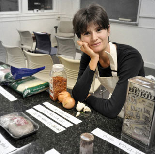 A woman poses in a kitchen with various items like olive oil, garlic and onions. A woman poses in a kitchen with various items like olive oil, garlic and onions.