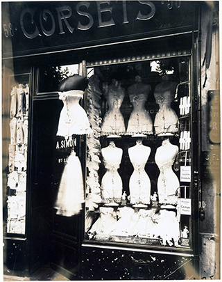 A shop window displaying rows of corsets on dress forms. A shop window displaying rows of corsets on dress forms.