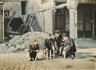 A group of four boys playing with multicolored wooden toys on a cobblestone street amidst rubble.