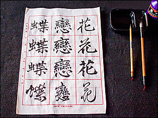 Three Chinese characters in four different calligraphy scripts written on calligraphy grid paper, with two brushes, a bottle of ink, and an inkstone at the side. Three Chinese characters in four different calligraphy scripts written on calligraphy grid paper, with two brushes, a bottle of ink, and an inkstone at the side.