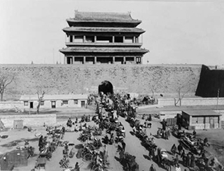 A black and white photo of a busy street scene in front of Hata-men gate, Beijing, China. A black and white photo of a busy street scene in front of Hata-men gate, Beijing, China.