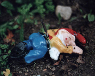 Ceramic figurine with red cap face down in the dirt with a knife in his back. Ceramic figurine with red cap face down in the dirt with a knife in his back.