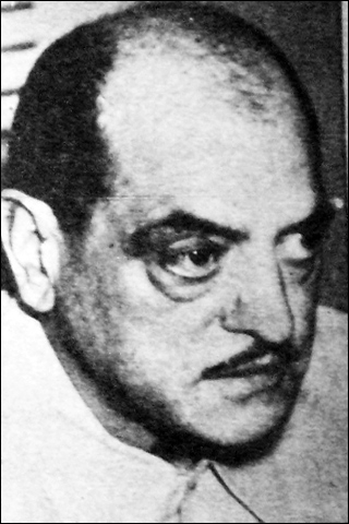 A black and white photograph of a man. He is balding and has a thin mustache. A black and white photograph of a man. He is balding and has a thin mustache.