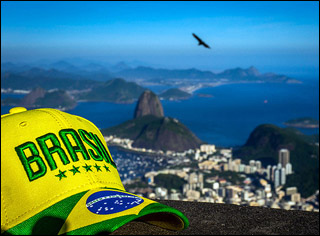A photograph with a cap that says "Brasil" in the foreground, with the view of the city and ocean in the background. A photograph with a cap that says "Brasil" in the foreground, with the view of the city and ocean in the background.