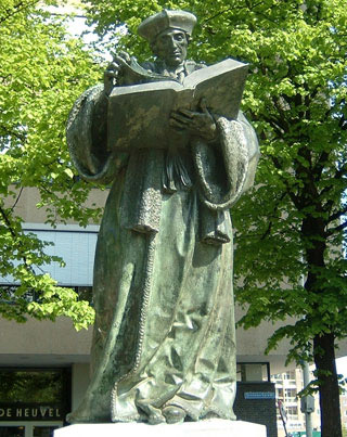 A statue of man wearing an elaborate robe and headwear, reading from a large book. A statue of man wearing an elaborate robe and headwear, reading from a large book.