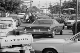 A black and white photo of cars and trucks lined up, surrounding a single gas pump. A black and white photo of cars and trucks lined up, surrounding a single gas pump.
