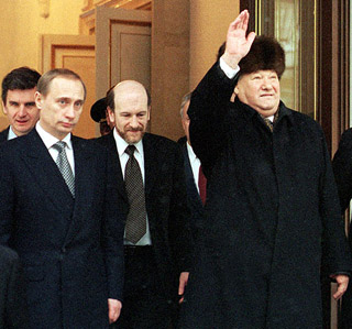 A grey-haired gentleman wearing a fur hat and black overcoat, raises his hand in a wave. A grey-haired gentleman wearing a fur hat and black overcoat, raises his hand in a wave.