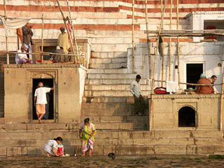 Women washing clothes, men gathered in groups, a flight of stairs ascending up from the riverbank. Women washing clothes, men gathered in groups, a flight of stairs ascending up from the riverbank.