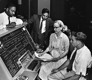 A black and white photograph circa 1960 with four people gathered around the UNIVAC I keyboard, which was the first commercial electronic computer. A black and white photograph circa 1960 with four people gathered around the UNIVAC I keyboard, which was the first commercial electronic computer.