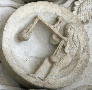A photograph of a stone sculpture of Libra and her scales on Autun Cathedral. A photograph of a stone sculpture of Libra and her scales on Autun Cathedral.