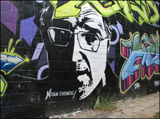 A mural on a brick wall depicts a half-lit bespectacled man's face, surrounded by multi-colored script. A mural on a brick wall depicts a half-lit bespectacled man's face, surrounded by multi-colored script.