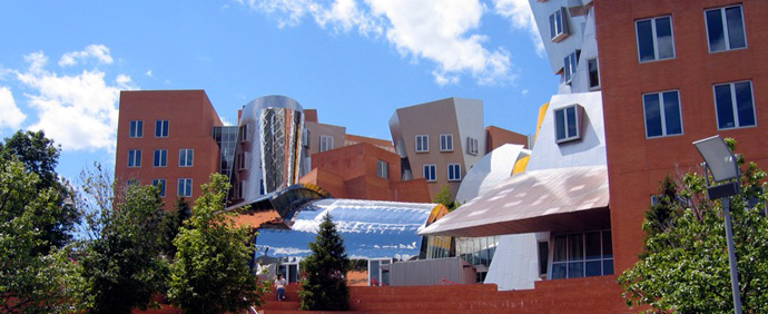 A photograph of the exterior of a building on the MIT campus on a sunny day. A photograph of the exterior of a building on the MIT campus on a sunny day.